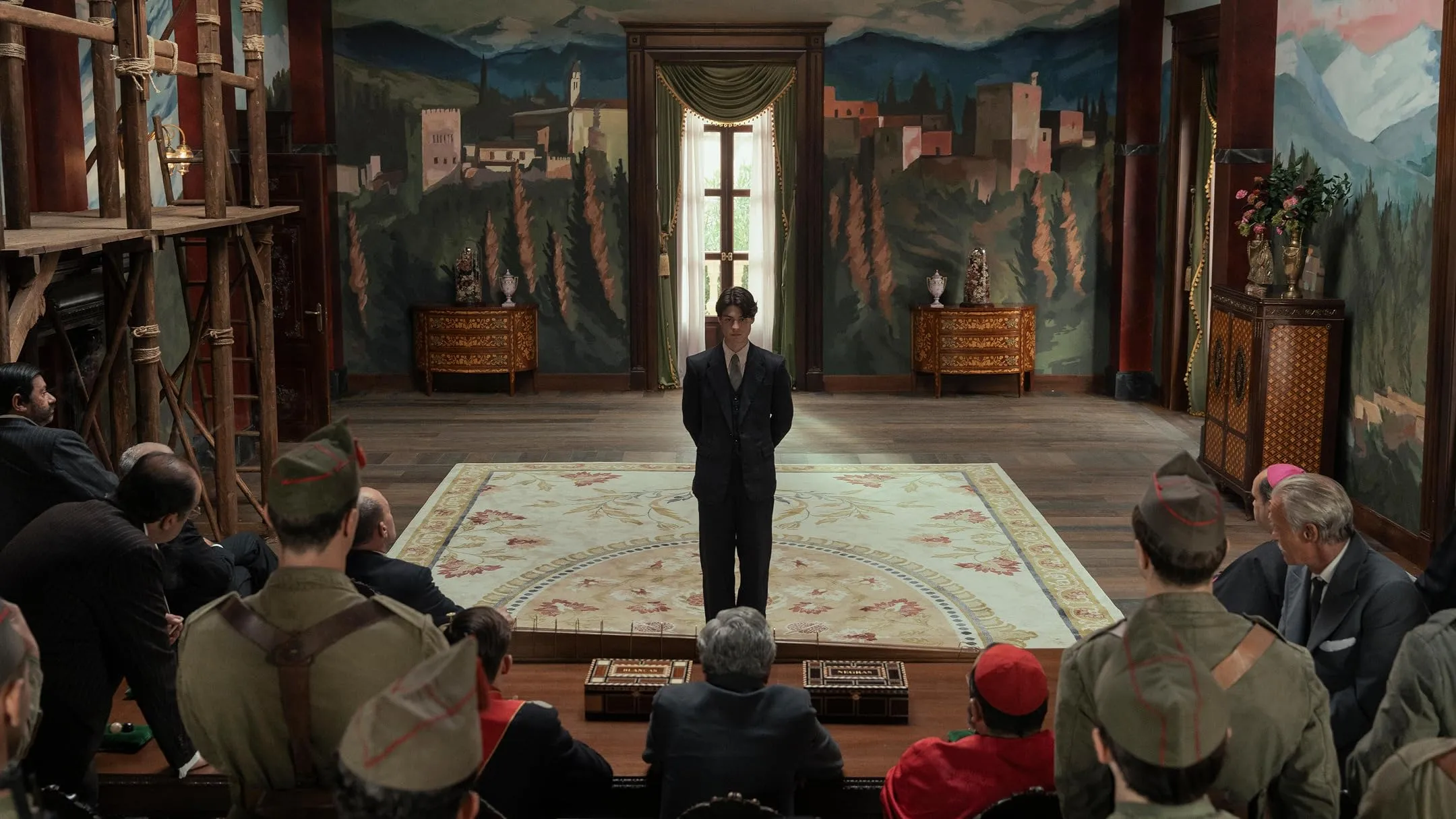 A man standing before a group of seated men in a room decorated with murals, in La Bola Negra